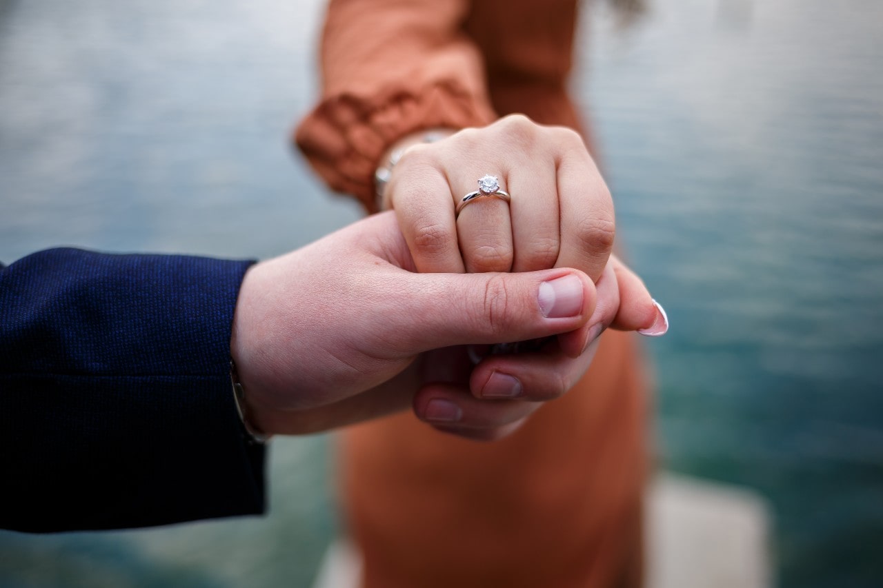 close up of a man holding a woman’s hand wearing an engagement ring