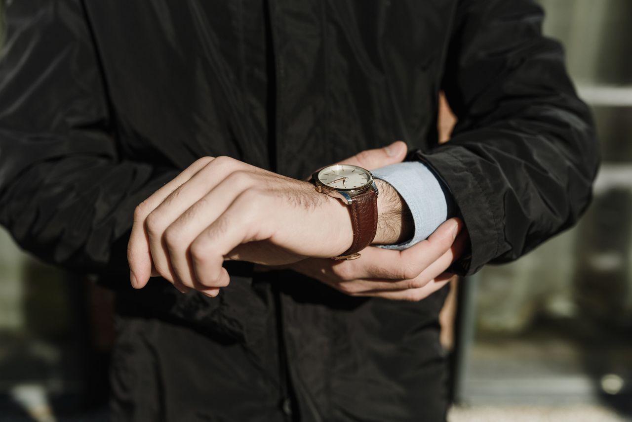 A man in a black jacket checks his watch while walking outside.