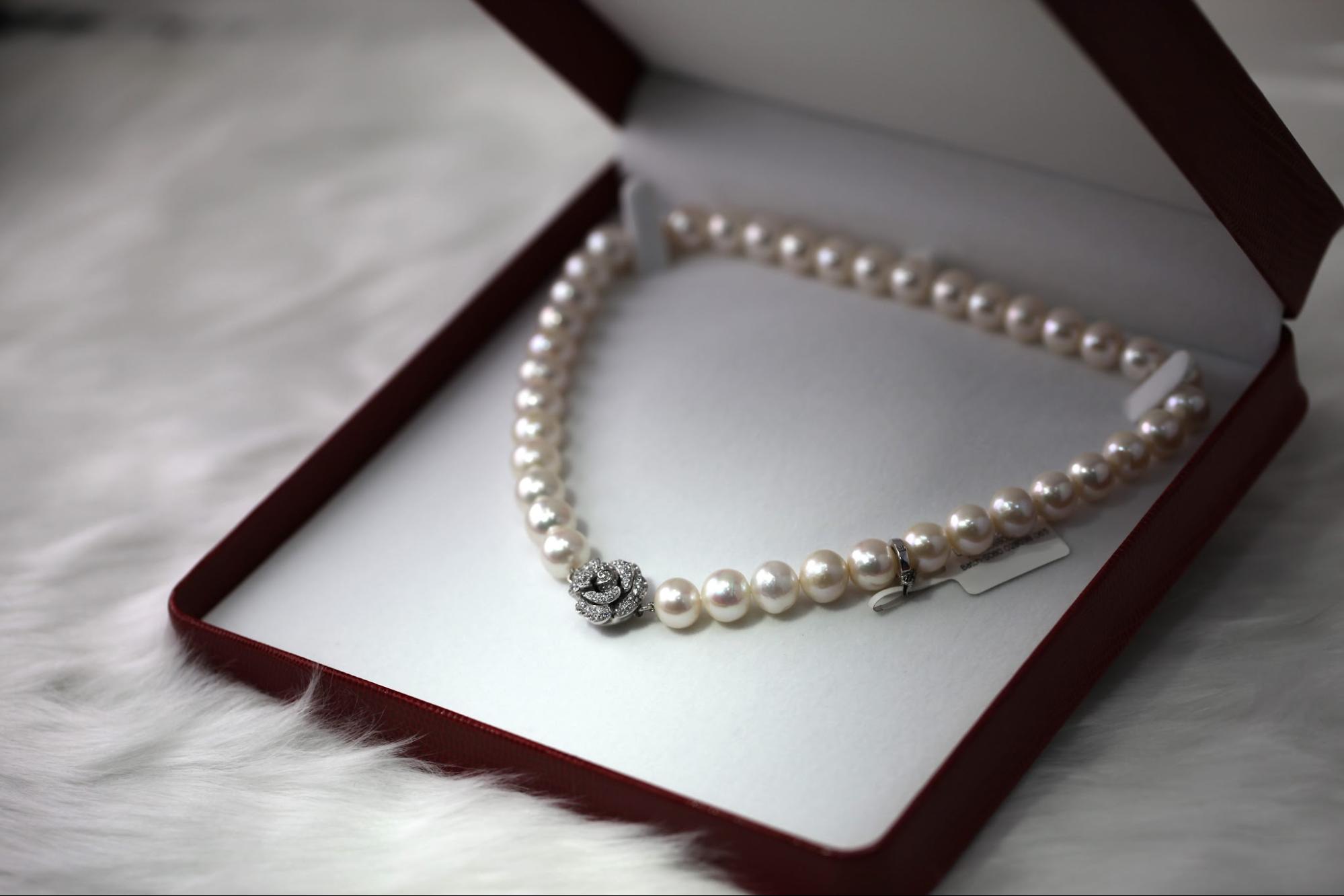 Close-up of a jewelry box displaying a pearl necklace with a floral diamond pendant.