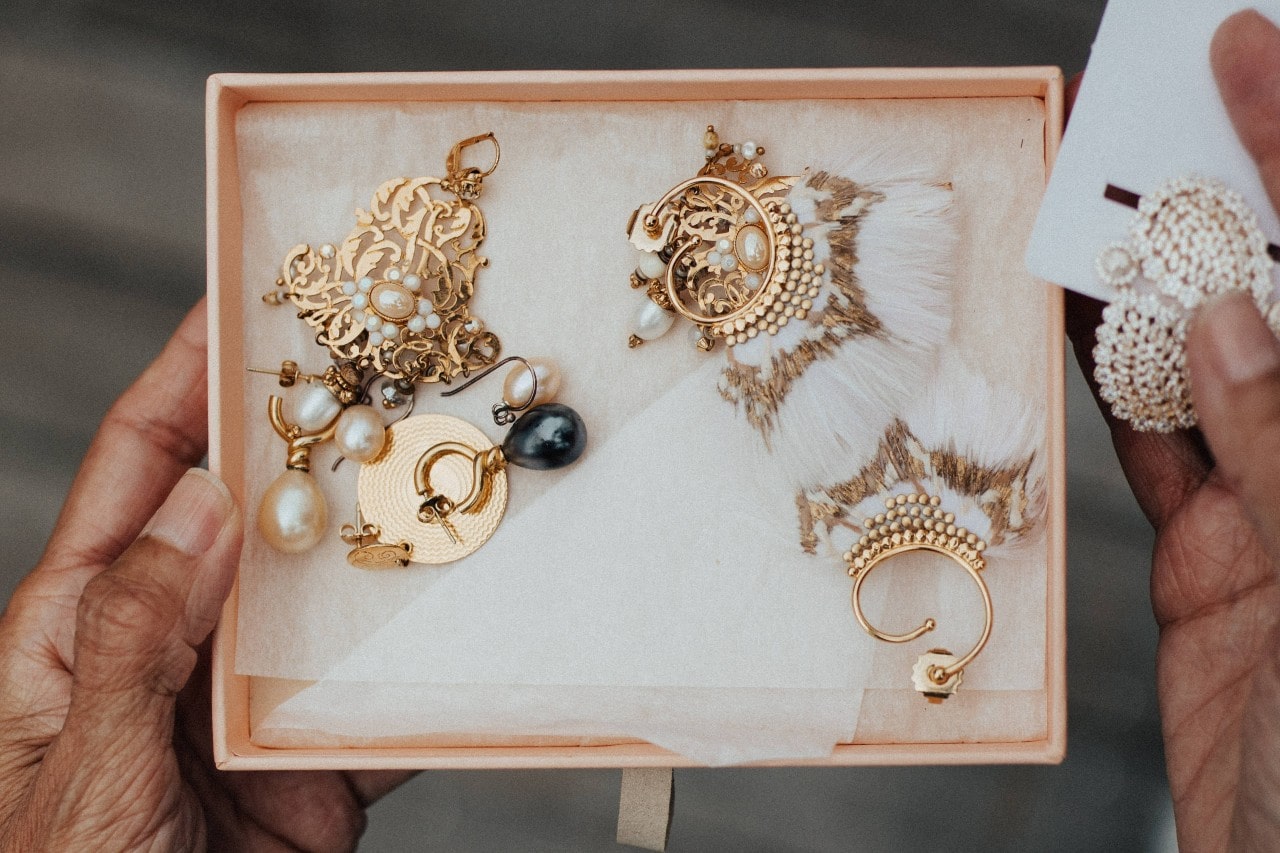 A person holding an open box with golden vintage earrings with feather accents.