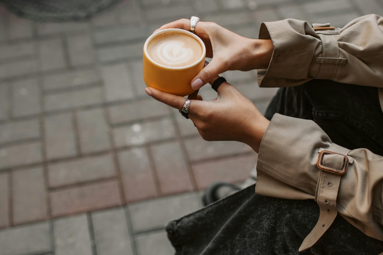 A woman holding a yellow latte glass, showcasing her chunky silver rings.