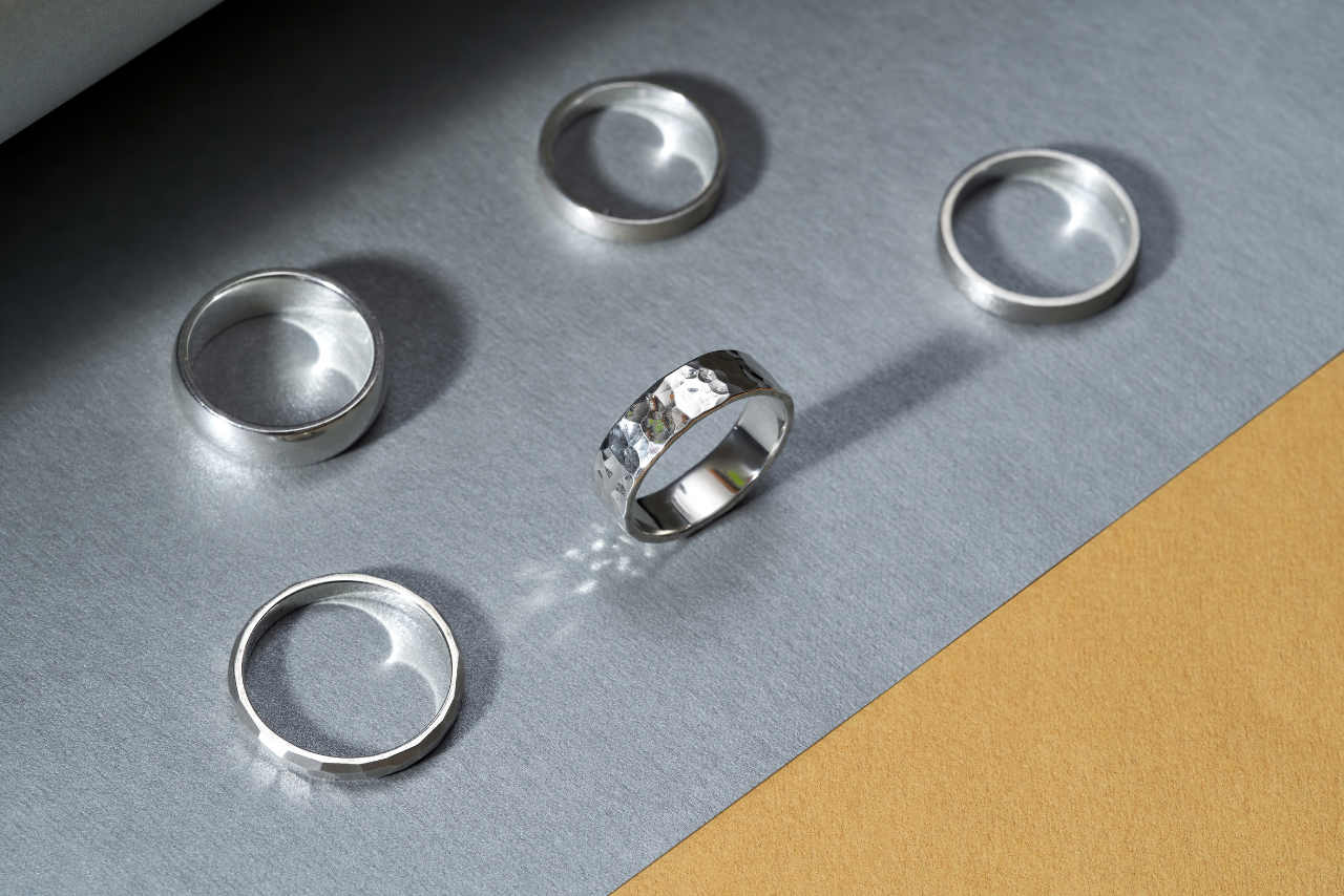 Five different silver rings sitting on a silver surface.