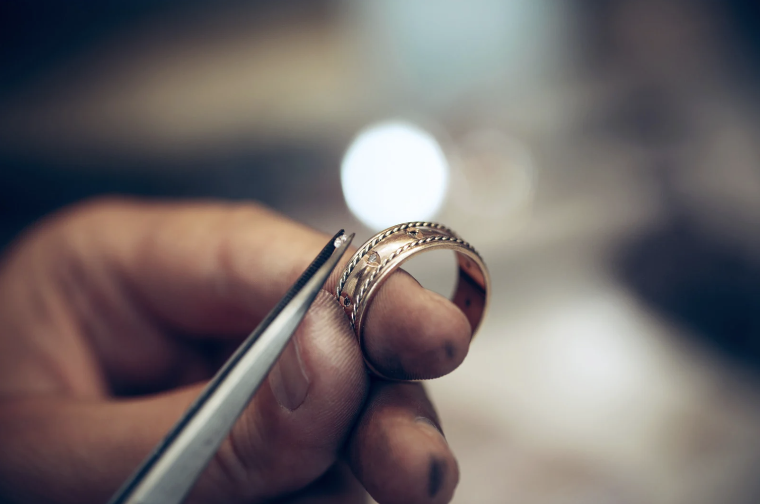 A jeweler working on a detailed rose-gold ring with diamond accents.