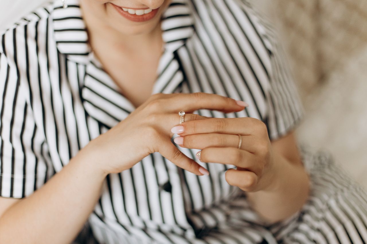 A woman wearing a black and white striped shirt smiles as she puts a diamond ring on her finger.