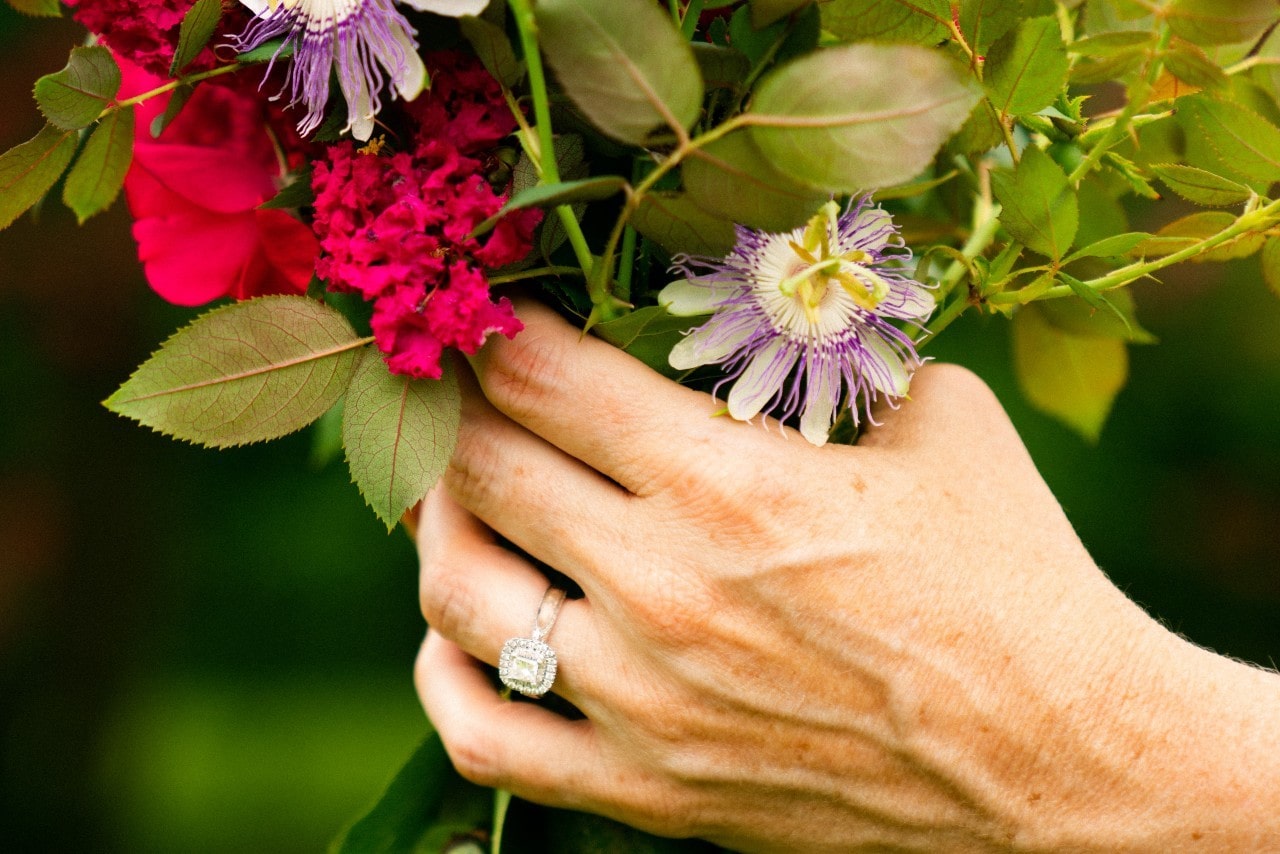 a woman’s hand holding a brightly colored bouquet and wearing a halo engagement ring