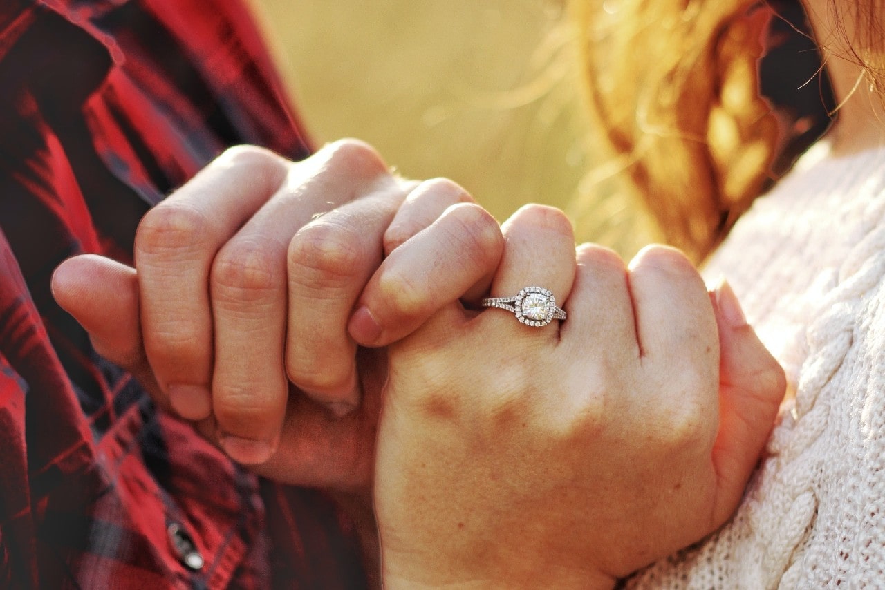 A closeup shot of a couple linking pinkies; the woman wears a halo engagement ring.