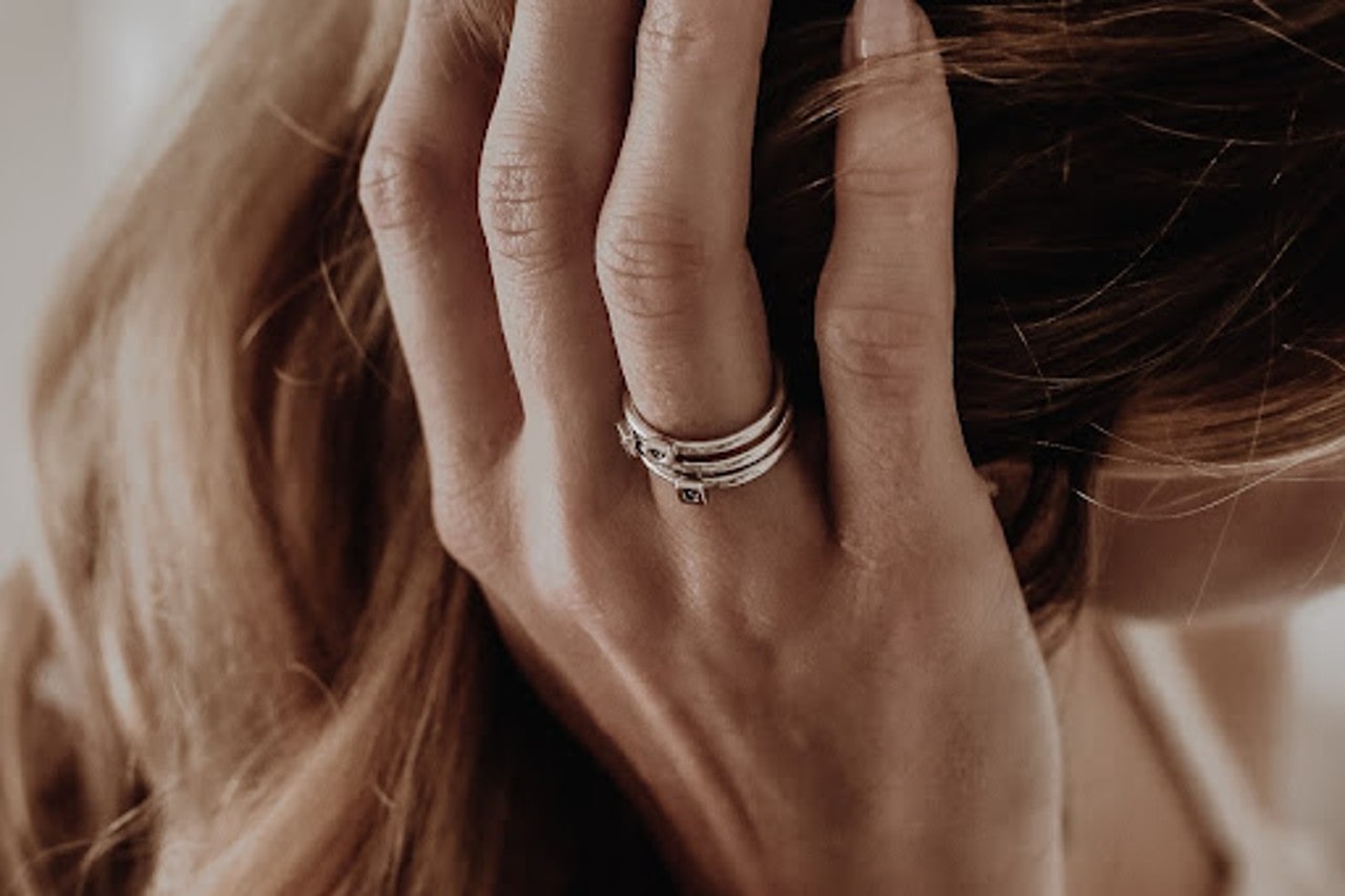 A trio of silver fashion rings on the hand of a woman who is running her hand through her hair