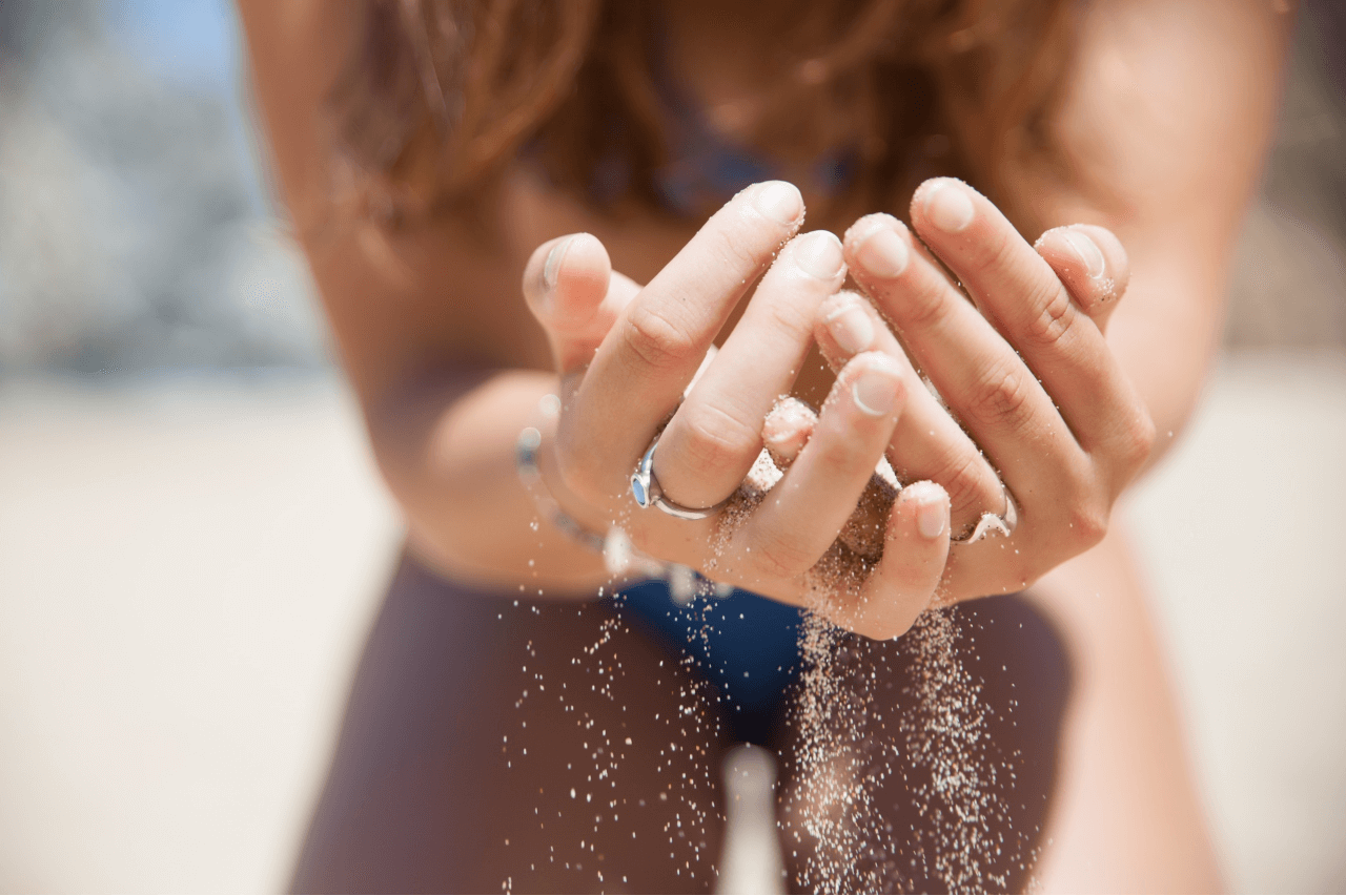 A woman letting sand fall from her cupped hands wearing multiple fashion rings