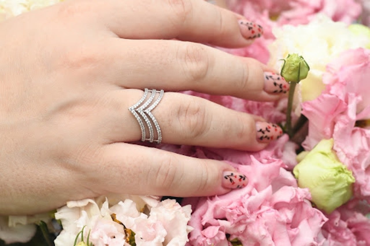 A hand with a multi-banded chevron ring with floral nails resting on a bouquet of flowers
