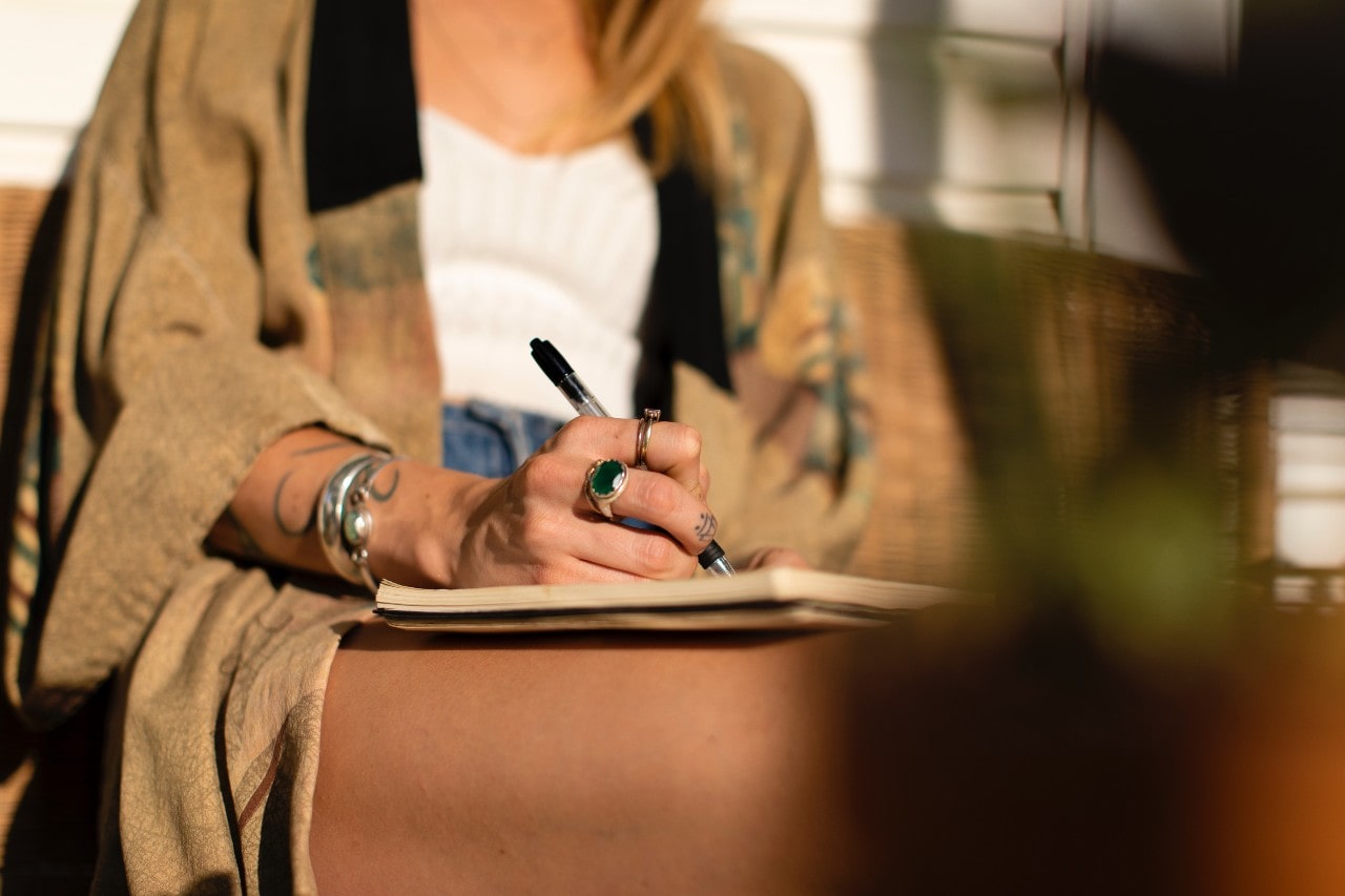 A woman sitting outside writing, wearing multiple rings.