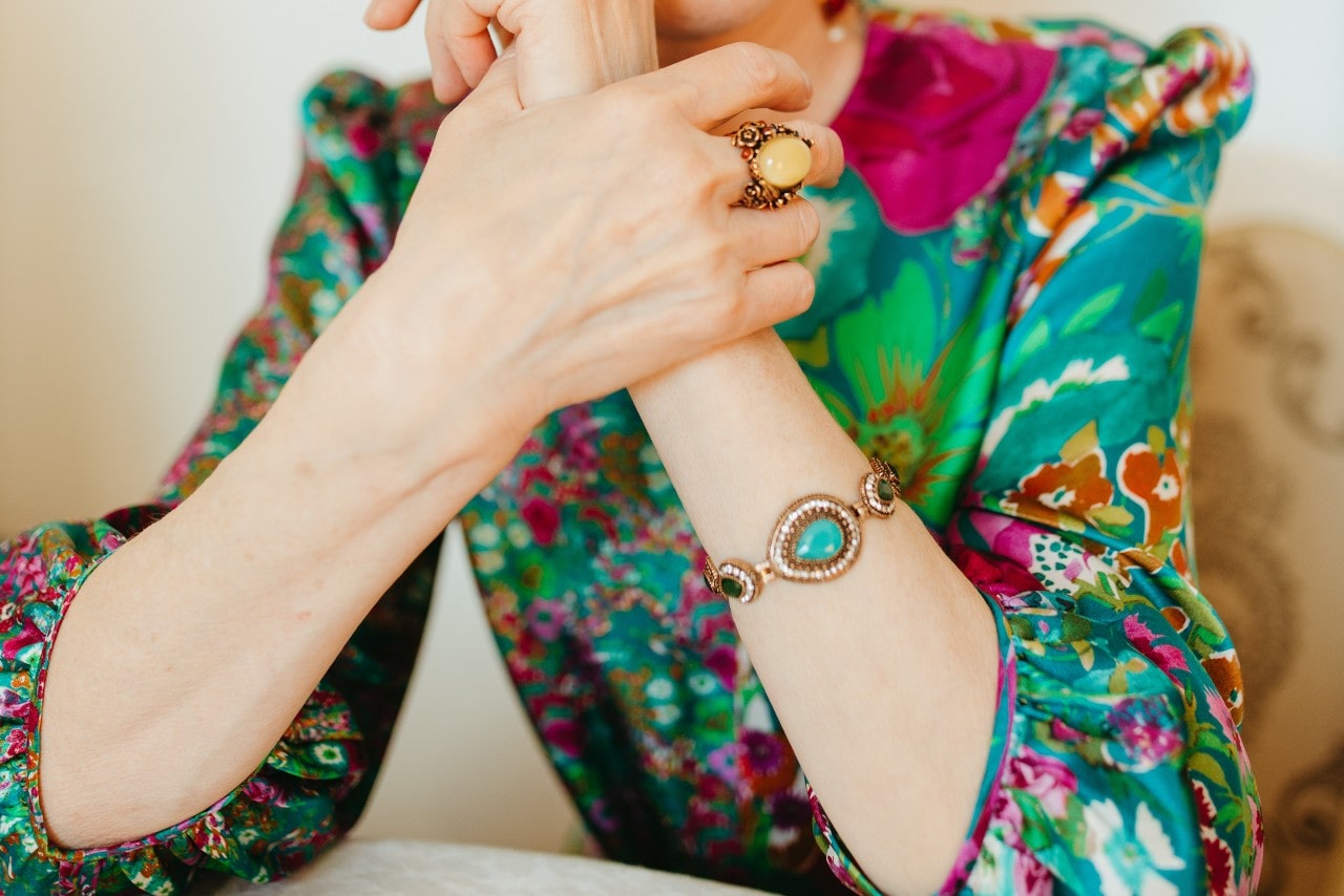 a woman in a colorful blouse wearing a turquoise and diamond bracelet and gemstone fashion ring