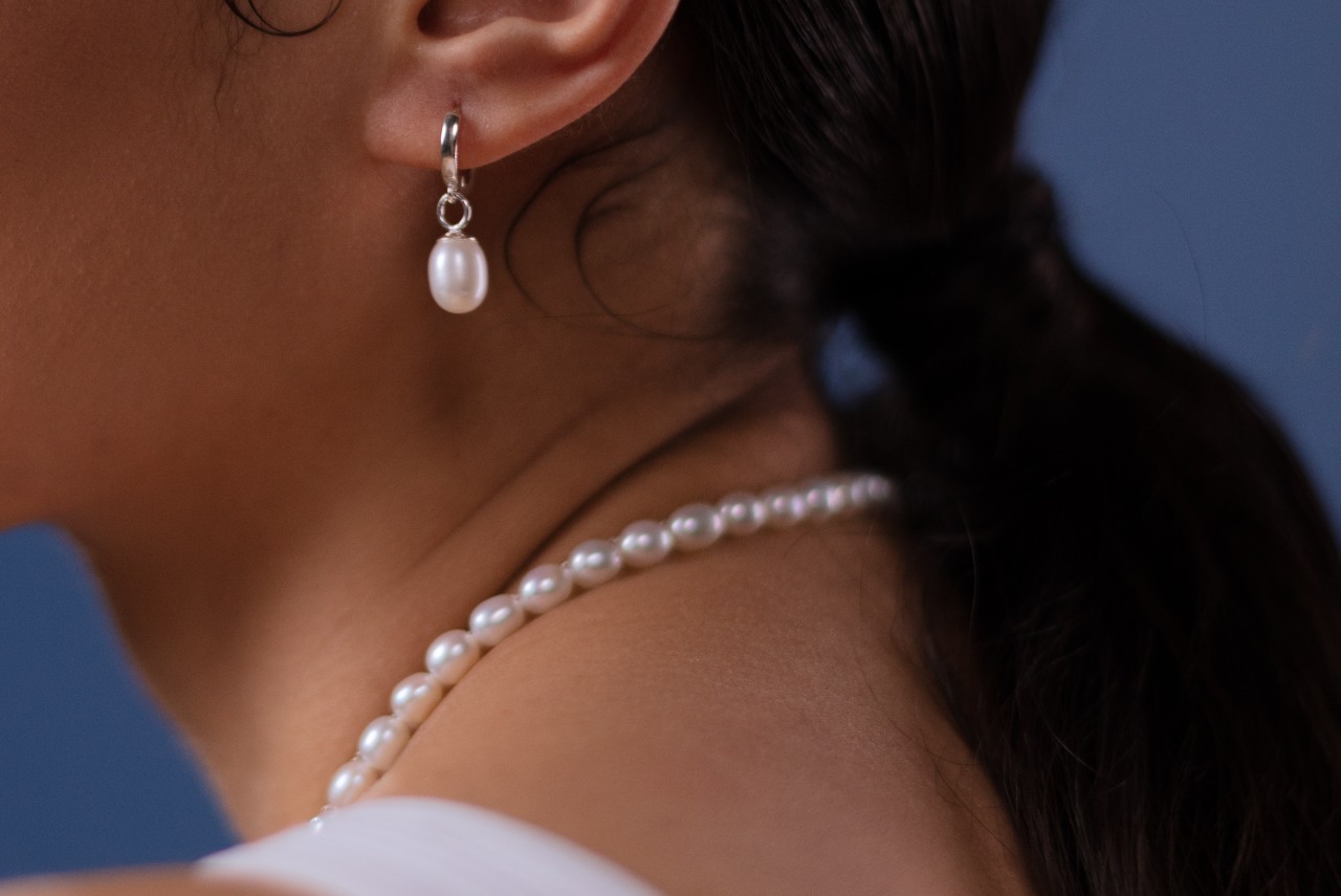 close up image of a woman wearing a pearl necklace and drop earring.