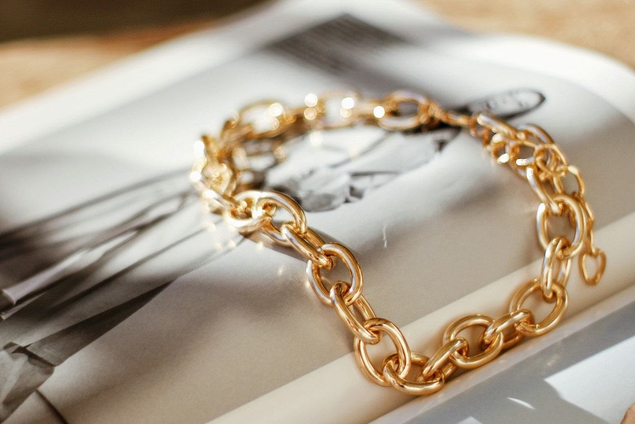A yellow gold chain bracelet with oval links rests on an open fashion magazine.