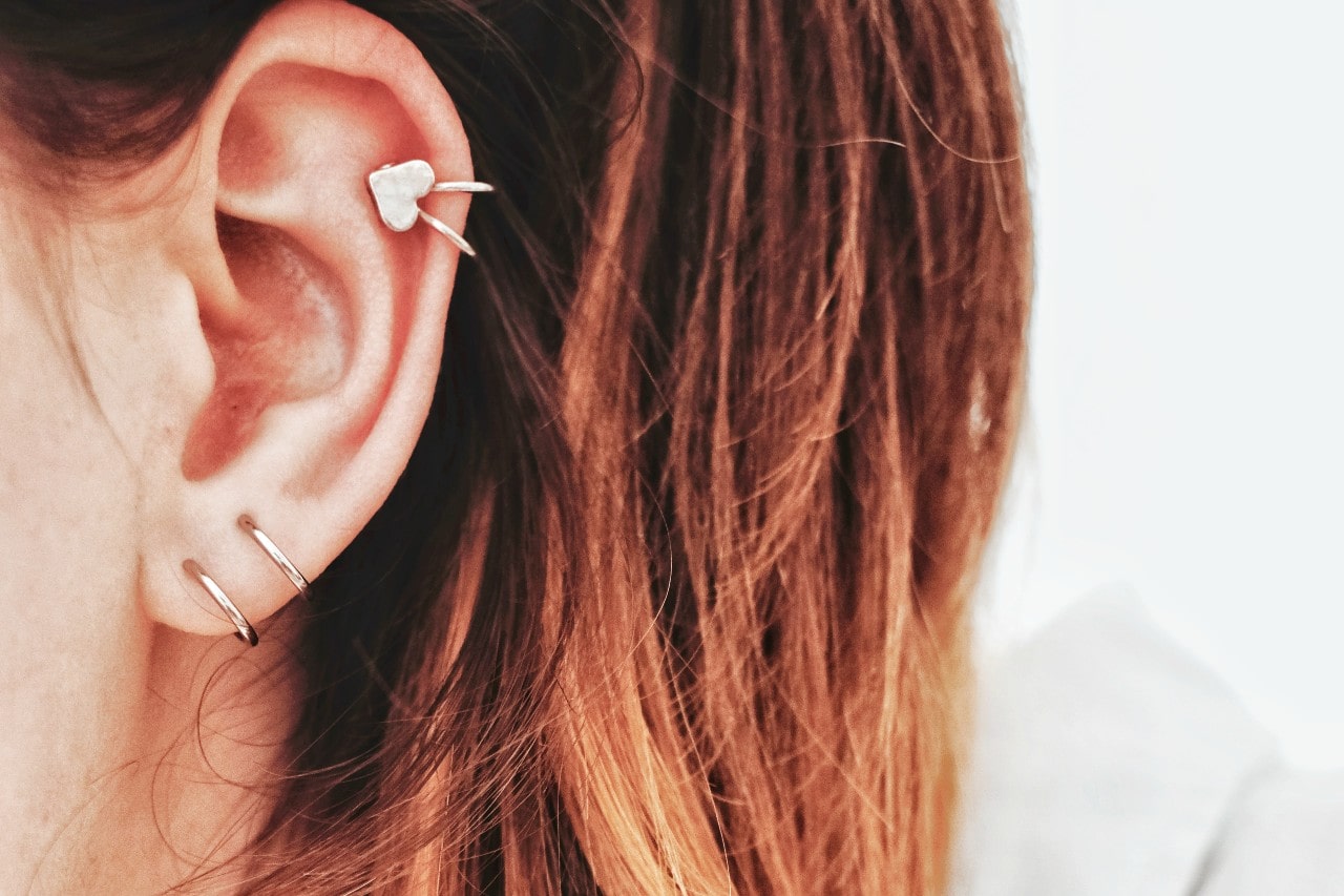 A close-up of gold hoops and heart huggie earring on a woman’s ear.