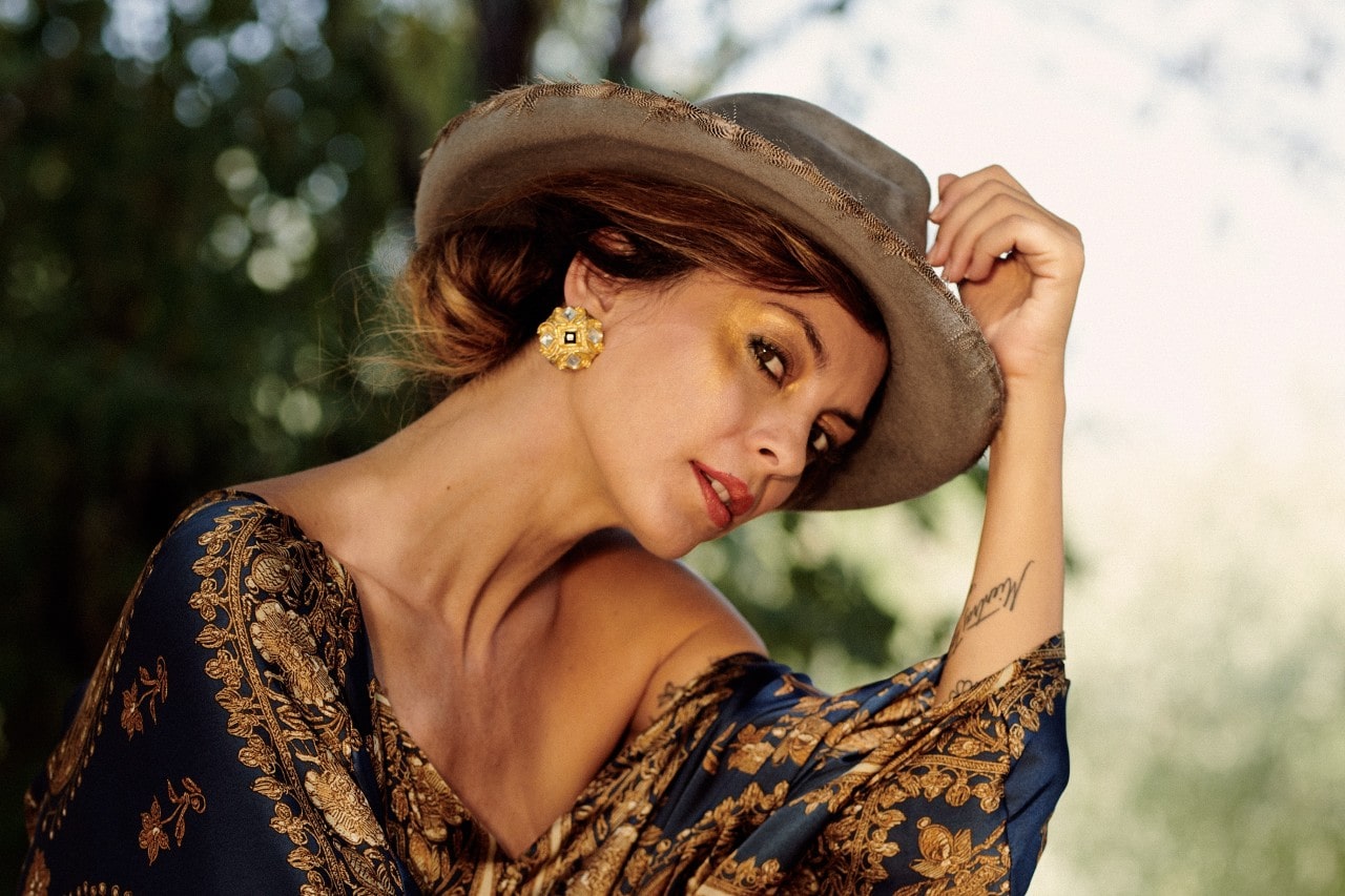 A woman with a fashionable hat poses for the camera, special emphasis on her large golden statement earring.