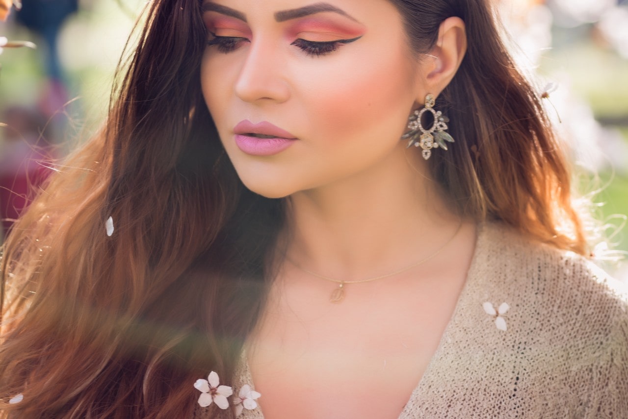 A woman with glamorous makeup wearing a large statement earring while the sun shines brightly on her face.
