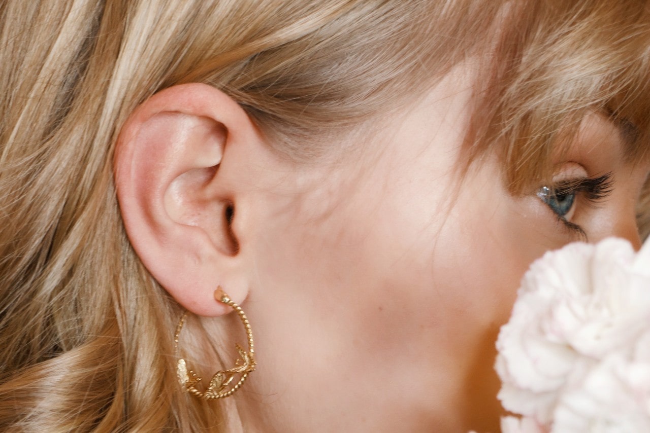 close up image of a woman’s face who is wearing a pair of detailed gold hoops