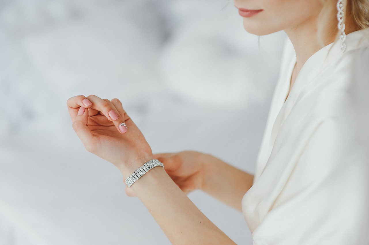 A woman in white silk robe fixing her white gold diamond bracelet