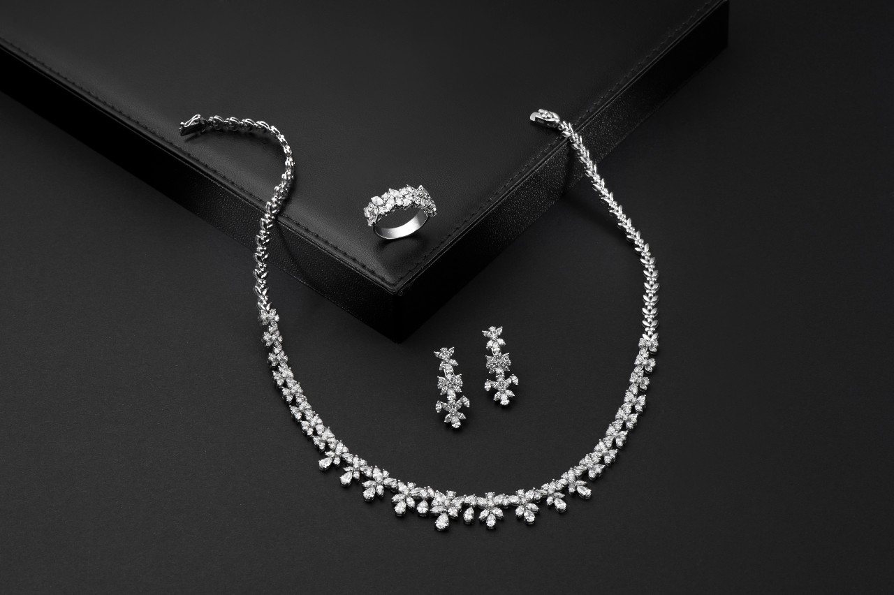 A close up of diamond necklace, drop earrings and fashion ring on a black surface