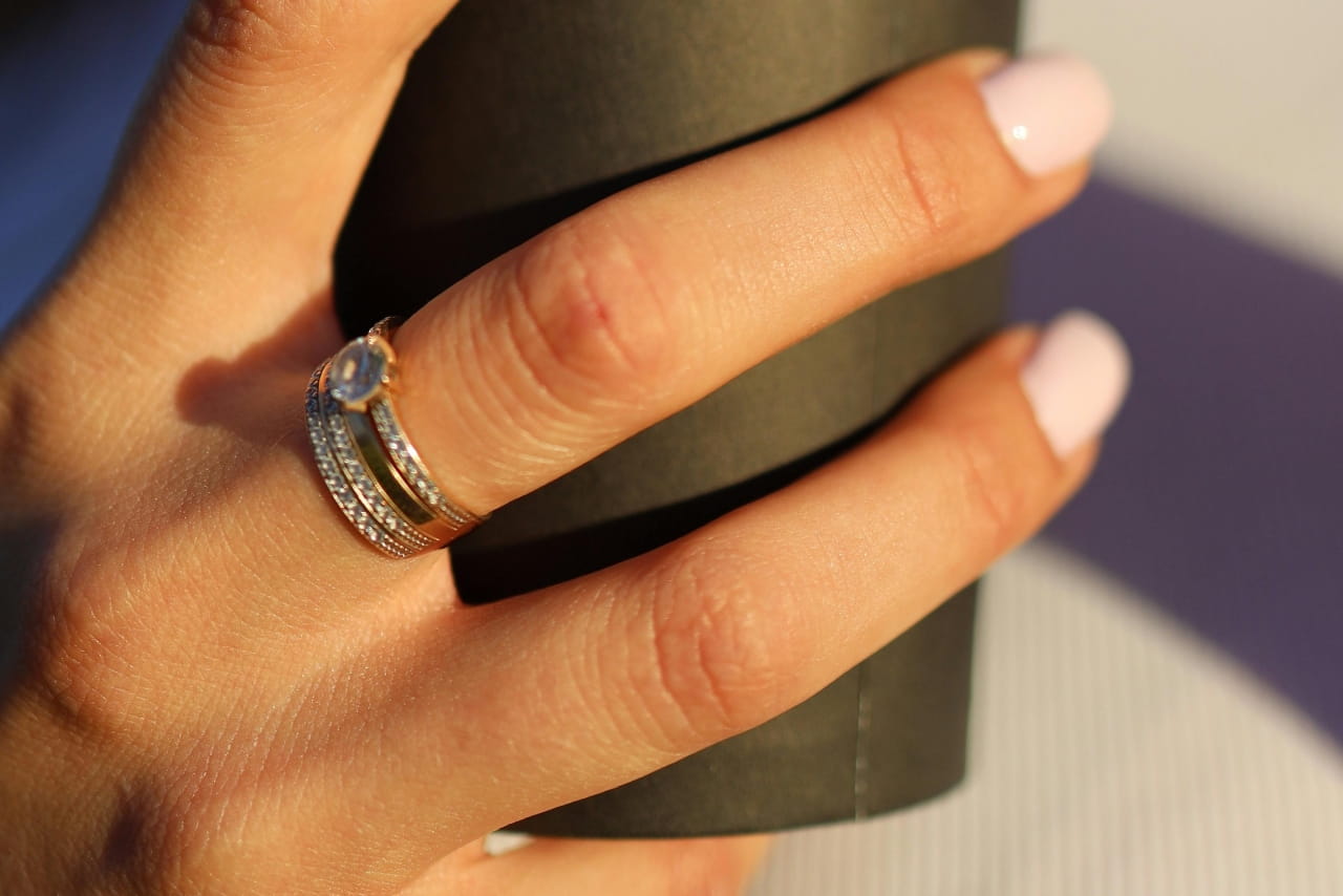 A close-up of a hand holding a paper cup with a white gold diamond wedding set on the middle finger.