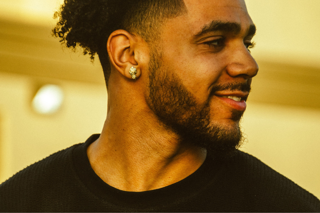A man smiling and looking off to the side, his diamond stud earring visible.