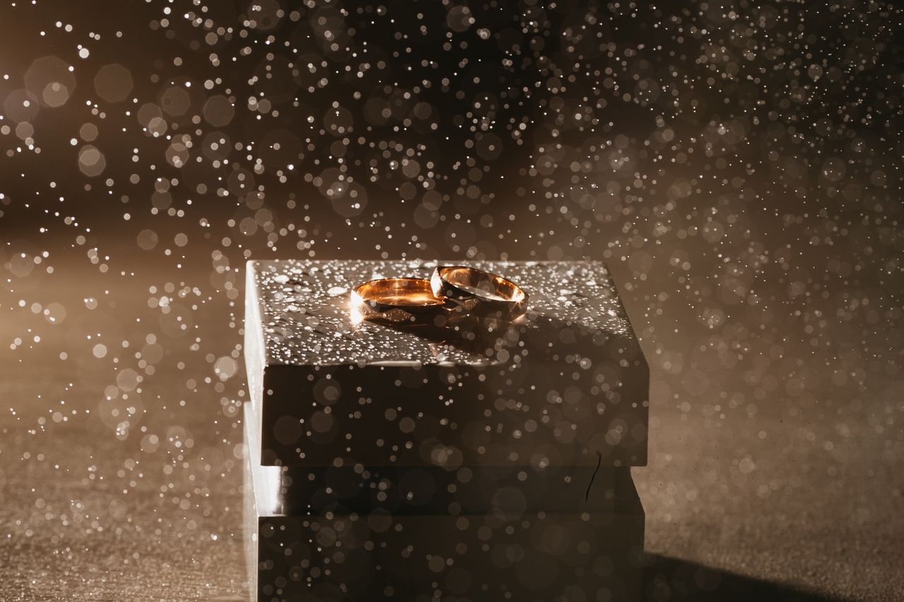 two gold men’s wedding bands sit on top of a ring box as mist pours over them.