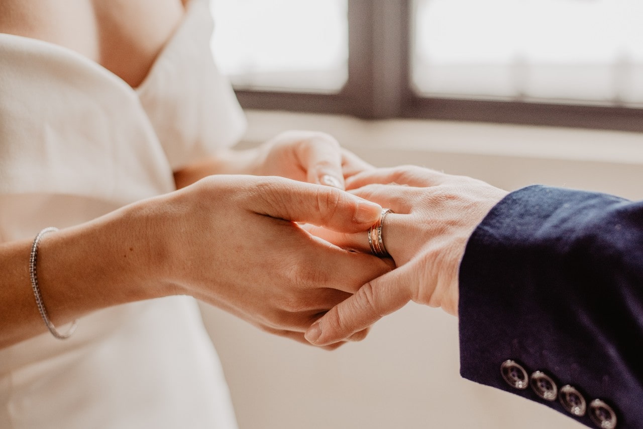 a woman slips a wedding band on her groom’s finger during a wedding ceremony.