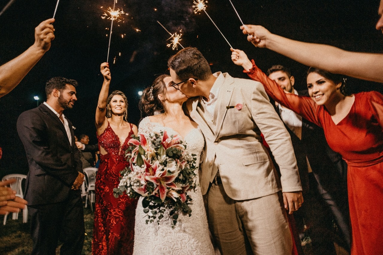 a newly-married couple kisses under a sparkler exit with their guests.