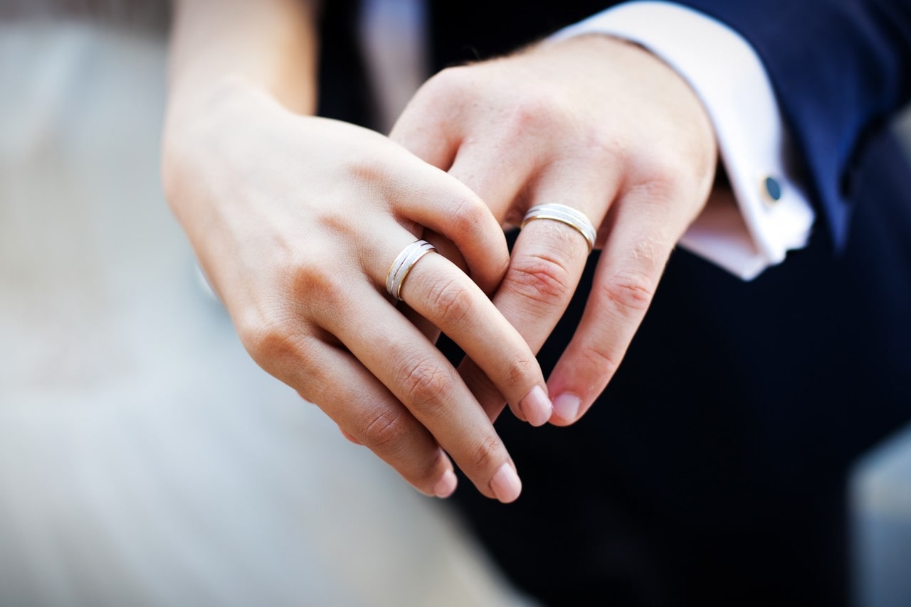 A close-up of a newlywed couple holding hands, with emphasis on their matching wedding bands. A close-up of a newlywed couple holding hands, with emphasis on their matching wedding bands.