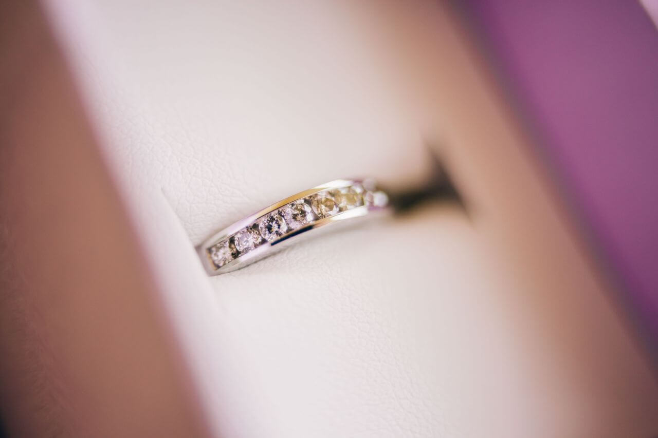 A close-up of a diamond-studded silver ring in a white, cushioned jewelry box. A close-up of a diamond-studded silver ring in a white, cushioned jewelry box.