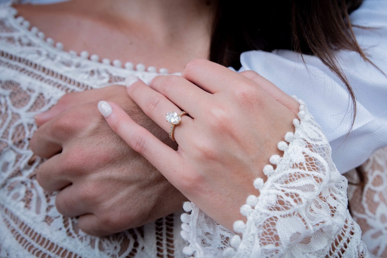 Woman’s hand wearing a diamond ring and holding a man’s hand
