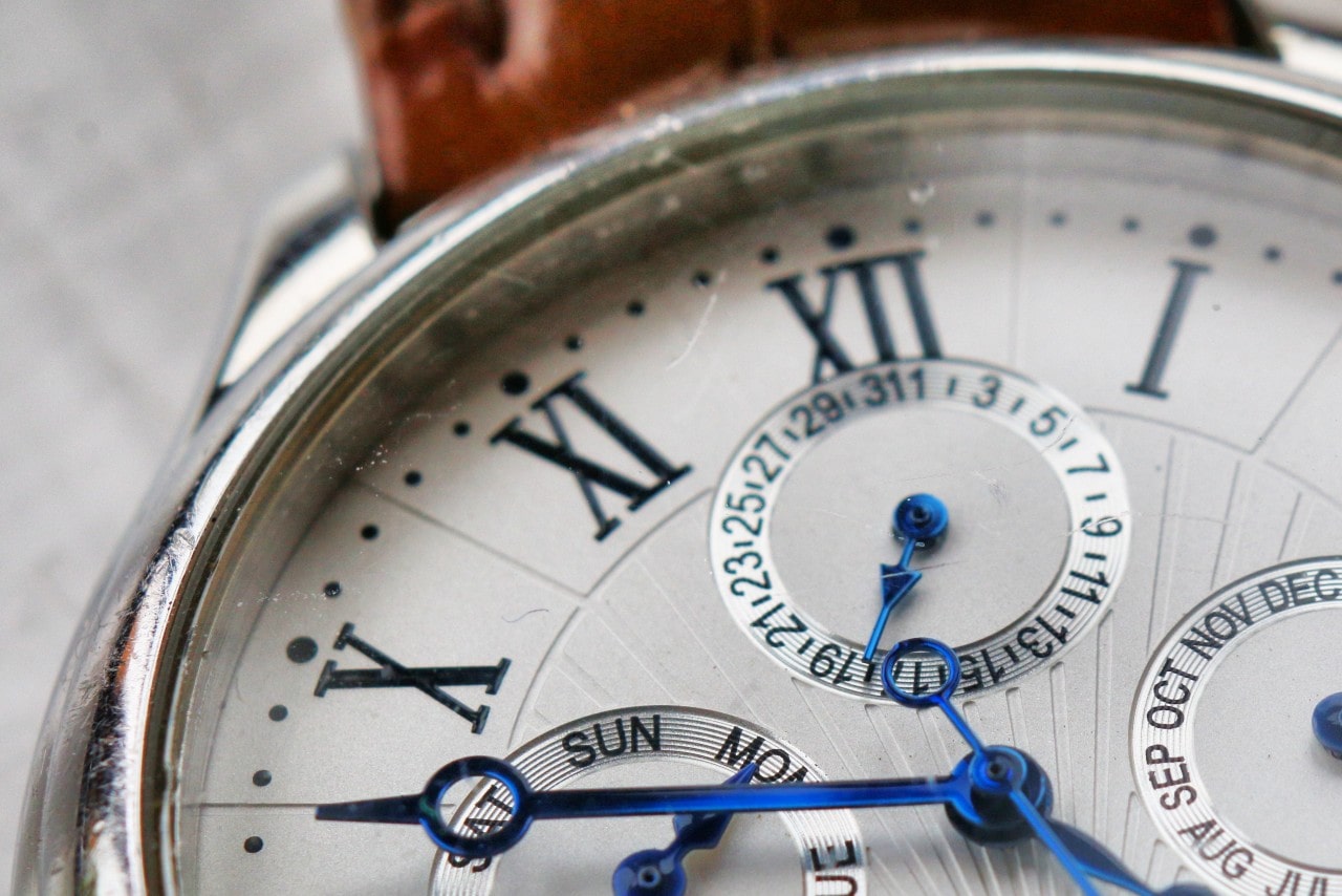 A close up of a white watch dial with roman numerals and deep blue hands.