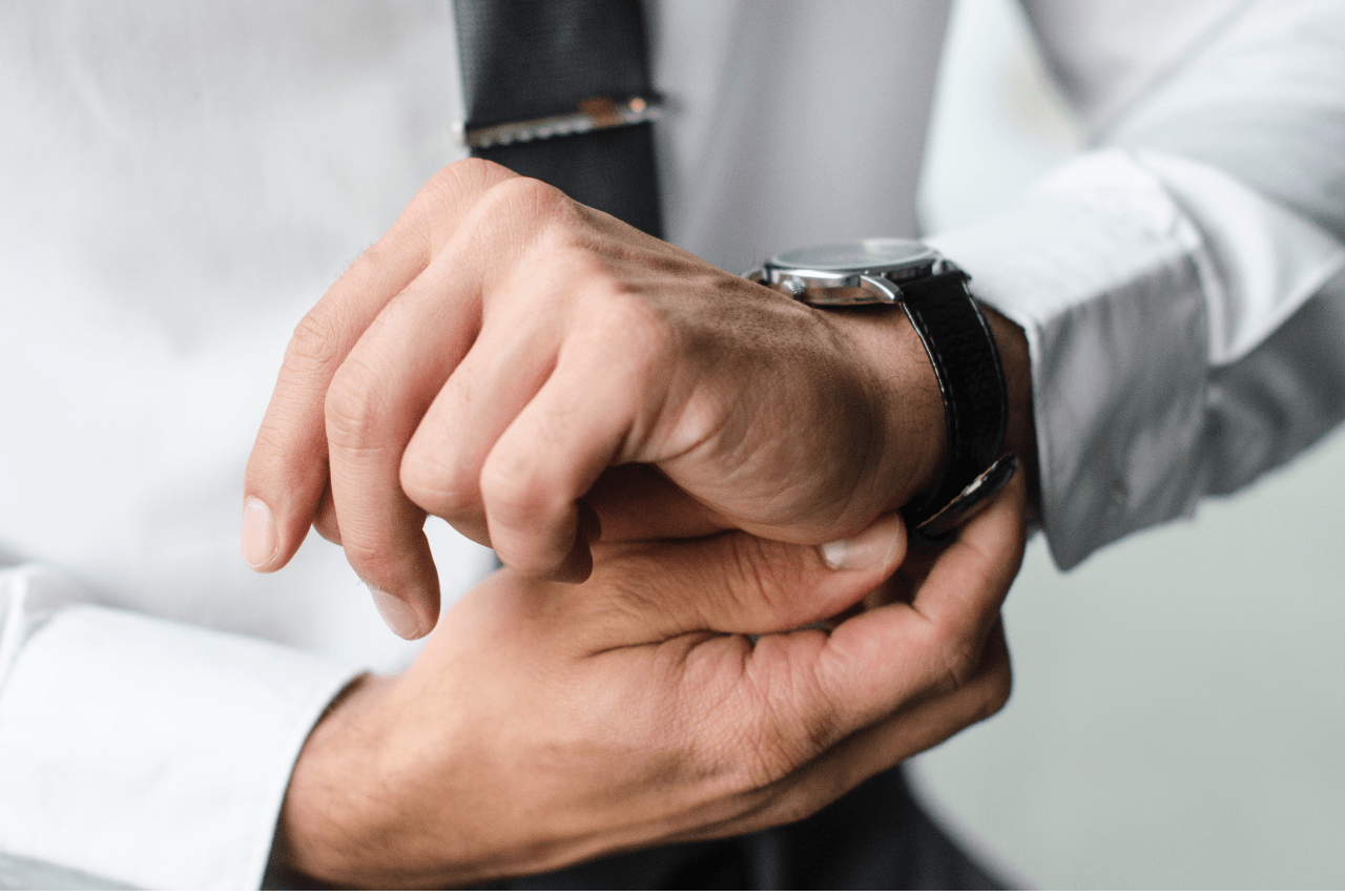 A man in white shirt fixes his black leather wristwatch.