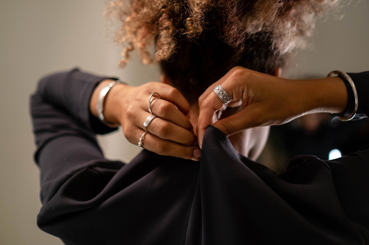A woman fastening black fabric around her neck, wearing platinum jewelry.