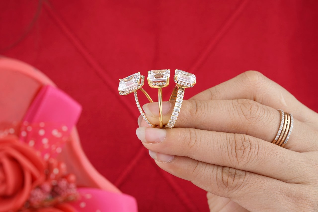 a lady’s hand holding three different styles of engagement ring