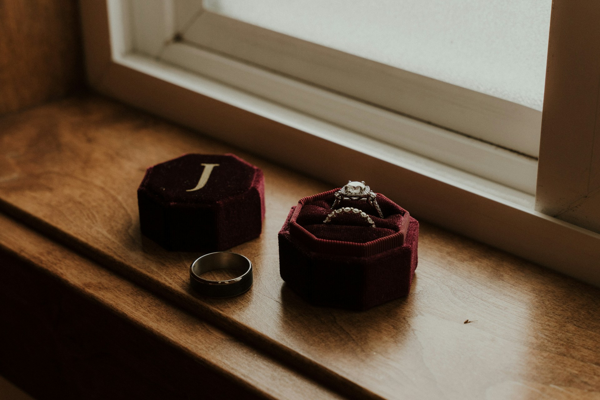 A ring box containing a bridal engagement ring and wedding band, next to a man’s wedding band on a windowsill. A ring box containing a bridal engagement ring and wedding band, next to a man’s wedding band on a windowsill.
