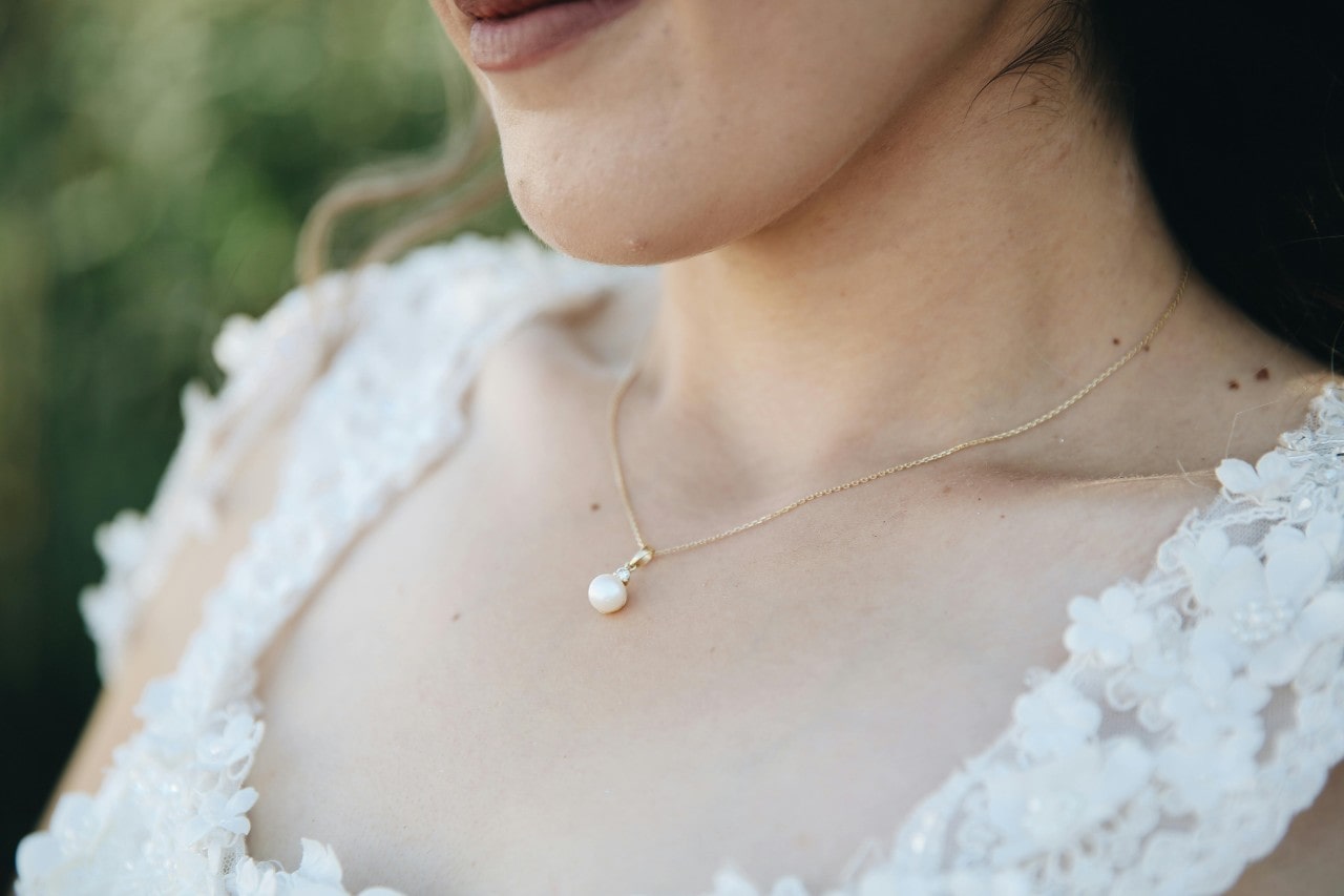 A bride’s neckline adorned with a simple pearl pendant necklace. A bride’s neckline adorned with a simple pearl pendant necklace.