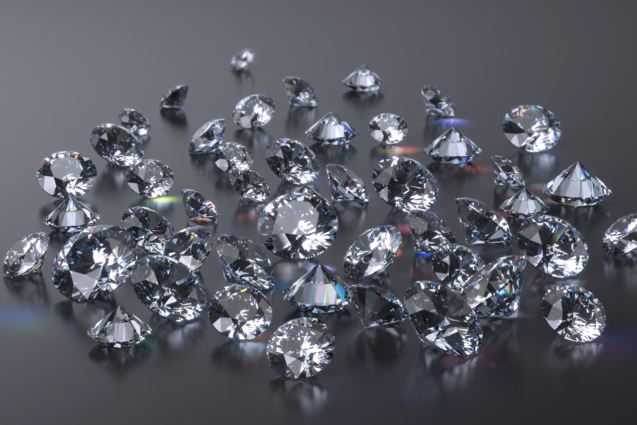A scattered collection of numerous round-cut diamonds displayed on a glossy dark surface.