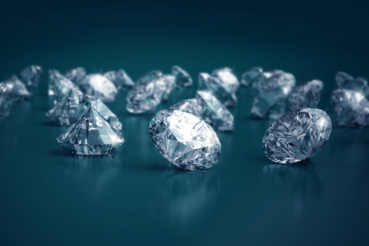 A group of sparkling, faceted diamonds is scattered across a glossy surface.
