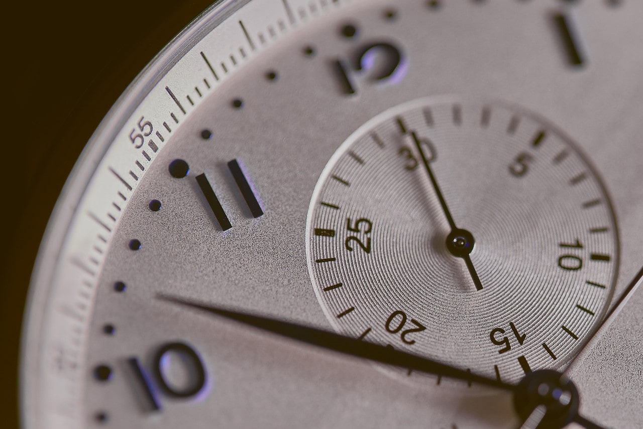 A close up of a white watch dial with purple arab numerals and complications.