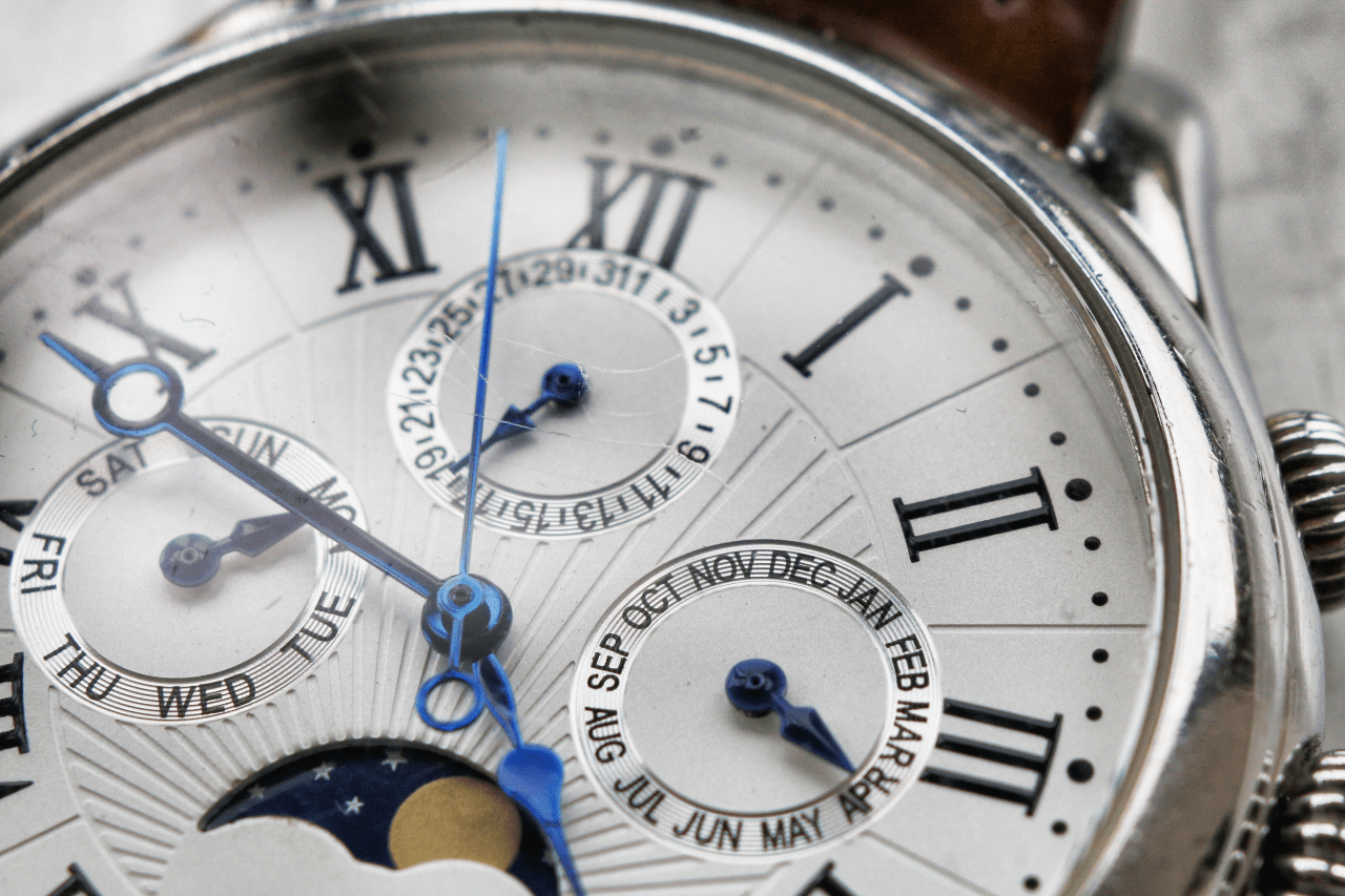 A close up of a white watch dial with roman numerals and several complications.